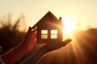 A symbol of your cozy home against the backdrop of the setting sun. Little wooden house in female hand delicately conveying dreams and hopes for secure.