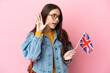Young French girl holding an United Kingdom flag isolated on pink background listening to something by putting hand on the ear