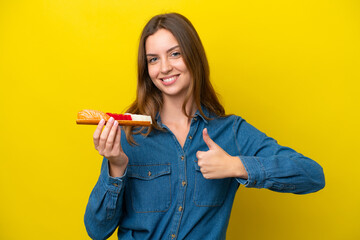 Wall Mural - Young caucasian woman holding sashimi isolated on yellow background with thumbs up because something good has happened