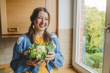 Happy Teenage Girl Holding Cauliflower Near Window At Home