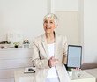 © Jelena Stanojkovic - Portrait of a mature businesswoman holding up a digital tablet with a blank screen in an home office.