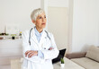 © Jelena Stanojkovic - Mature female doctor standing in her office in hospital. Older mature practitioner woman, posing indoors, looking away, thinking. Senior medical professional, doctor in white uniform casual portrait.