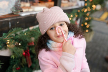 Smiling Girl Holding Candy Cane Over Face At Christmas Market