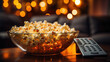 Close up bowl of popcorn and remote control with TV running in the background. Relaxing evening watching a movie or TV series at home.