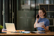 © Wasana - Businesswoman talking on the phone with friend or colleague while checking documents in modern office