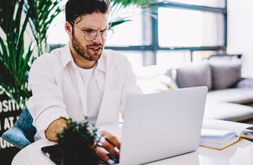Poster - Pensive caucasian male in spectacles checking news from networks working remotely at home