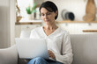 © fizkes - Serious middle-aged woman using laptop seated on sofa, web surfing helpful information, chatting on-line, buying services, lead correspondence to client working on weekend at home using internet. Tech