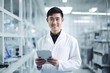 Portrait of Asian young man in white coat holding digital tablet smiling at camera while standing in the lab