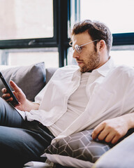 Poster - Concentrated millennial man searching phone number on mobile resting at home interior,