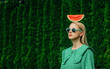 © VISTA by Westend61 - Woman wearing sunglasses standing with watermelon on head in garden