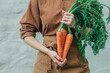 © VISTA by Westend61 - Woman holding bunch of carrot with leaves in front of wall