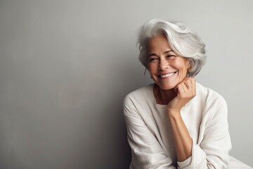 Portrait of beautiful mature woman with snow-white smile, gray hair on gray background. Middle-aged lady in light clothes, happy pensioner looking at the camera. Beauty, skin care concept