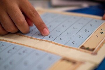 Hand of asian kids learning how to read the Holy Koran. Selective focus, grainy concept.