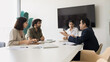 © fizkes - Serious diverse business colleagues discussing work on project, management strategy, meeting at table in boardroom. Young Indian leader woman holding negotiation of partners