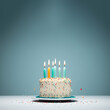 © Surachetsh - A tasty birthday cake with many colorful lit candles and decorated with rainbow sprinkle is isolated on the blue  white background. Generative AI.