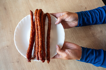 The woman holds food in her hand. The girl holds kabanos sausages on a plate. Sausages in hand.