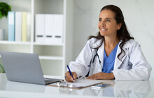 Smiling Mature Woman Doctor Taking Notes In Medical Chart
