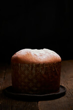 A Freshly Baked Panettone Sits On A Rustic Wooden Table, Highlighted Against A Dark Background, Creating An Intimate And Inviting Scene