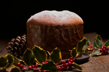 A Beautifully Presented Traditional Panettone With A Light Dusting Of Icing Sugar, Set Against A Backdrop Of Festive Decor Including Holly Berries And Pinecones