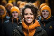 Cheerful young woman in orange beanie smiling brightly, surrounded by a happy group in matching winter attire.