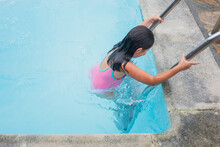 Girl In A Pink Swimsuit Climbing The Pool Ladder.