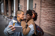 © Marko Geber - Young mixed lesbian couple taking a selfie on the smartphone while having a stroll together in the city