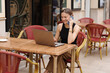 Successful smiling young business woman communication at smartphone during works on laptop at cafe outdoors. Concept of remote work from public place, digital freelance and modern lifestyle