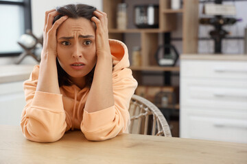 Poster - Beautiful young afraid woman sitting at table in kitchen