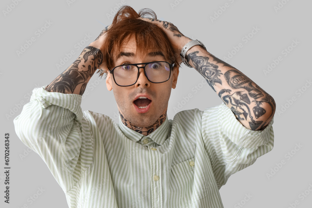Afraid young tattooed man on grey background