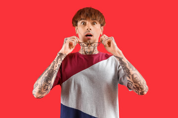 Wall Mural - Afraid young tattooed man on red background