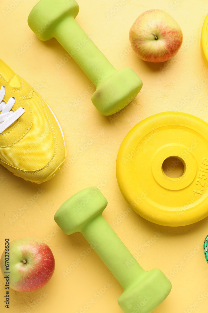 Barbell plate, apples and dumbbells on yellow background
