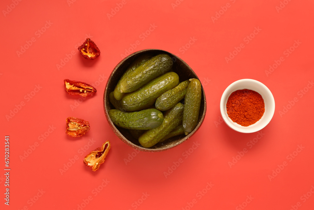 Composition with delicious fermented cucumbers in bowl and spices on red background
