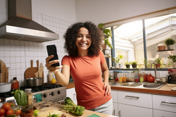 An adult latin woman is is making a selfie while smiling with a profesional camera in a kitchen while cooking a high tech social media woman