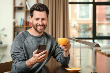 Canvas Print - Handsome man with cup of coffee using smartphone at table in cafe