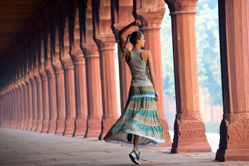 
A young woman with blond hair dances in a historical corridor with colorful columns, showing the beauty of architecture and fashion.