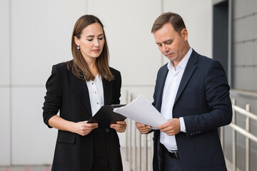 Concentrated businesswoman and businessman discussing critical business matters while reviewing documents at meeting. Business partners talk