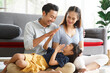 © aekkorn - Portrait of a happy young family. Mom, dad and daughter look each others and smile sitting on floor in living room. The faces of Asian parents and their child.