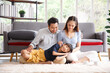 © aekkorn - Portrait of a happy young family. Mom, dad and daughter look each others and smile sitting on floor in living room. The faces of Asian parents and their child.