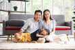 © aekkorn - Portrait of a happy young family. Mom, dad and daughter look each others and smile sitting on floor in living room. The faces of Asian parents and their child.