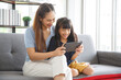 © aekkorn - Happy young asian mom and daughter using digital tablet, watching videos or surfing internet, sitting on sofa at home, copy space. Family,love and happiness concept.