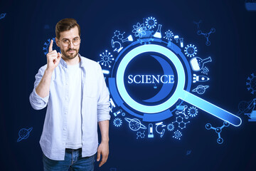 Poster - Attractive young european businessman pointing up at creative glowing magnifier hologram on blue background. Science, research and medicine concept.