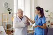© Studio Romantic - Doctor supporting her senior patient with an arm injury. Friendly young woman in blue uniform scrubs talking to a happy old man with a broken arm. Medical help, injury treatment concept