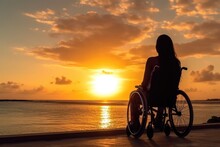 A Girl In A Wheelchair Sits On The Beach And Admires The Sunset