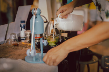 Barista preparing matcha latte with hand pouring milk in cafe.