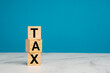 © meeboonstudio - Three wooden blocks with the letters 'TAX' are stacked on a marble table against a blue background
