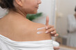 Spa Retreat: woman pampers her shoulder with moisturizing cream, creating a serene at-home spa moment. 