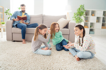 Canvas Print - Full size portrait of four persons positive guy hold book small girls sit on carpet communicating enjoy weekend indoors