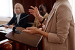 © AnnaStills - Cropped shot of young female witness in beige blazer standing by tribune with microphone and testifying in front of jury, judge and protection side