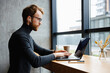 © YURII MASLAK - A young red-haired guy, a programmer or entrepreneur in glasses, works in a stylish cafe behind a laptop. Freelancer works remotely. Online communication. Small business.