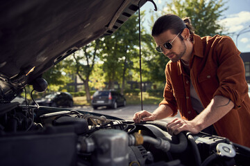 Wall Mural - thoughtful young sexy driver with sunglasses and beard looking attentively at his car engine